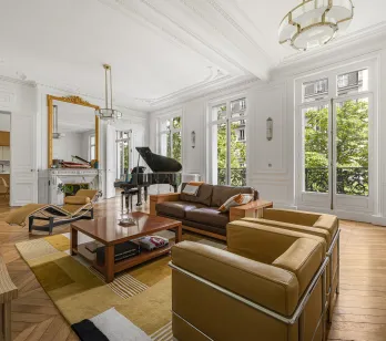 Salon Haussmannien de luxe à Paris: piano, parquet, moulures, cheminée, vue verdoyante. Élégance et lumière.