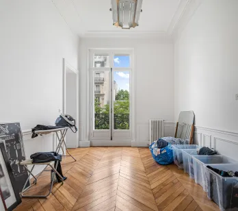 Appartement haussmannien Paris. Pièce lumineuse, parquet chevrons, moulures, fenêtre balcon. Potentiel luxe, vue verdoyante.