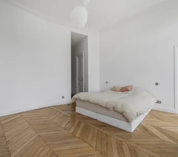 Chambre luxe minimaliste, parquet chevron, murs blancs. Élégance parisienne, luminosité naturelle. Idéal appartement haussmannien.