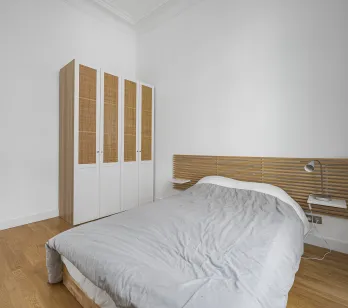 Chambre moderne et lumineuse avec parquet, tête de lit design en bois, et armoire élégante en rotin. Idéal pour appartement de luxe.