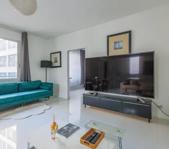 Salon moderne et lumineux avec canapé velours bleu canard, grand écran TV, design épuré. Idéal pour un appartement de luxe urbain. Confort et style.