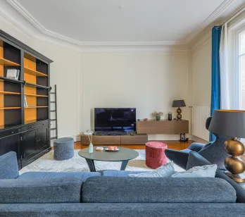 Salon parisien élégant et lumineux avec bibliothèque intégrée, canapé design et TV. Idéal pour un appartement de luxe.