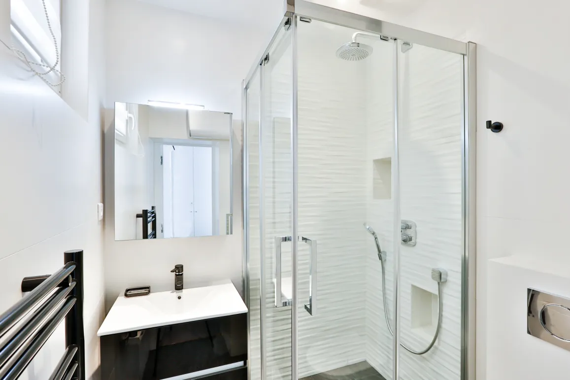Salle de bain moderne et lumineuse avec douche à l'italienne, vasque design et miroir. Luxe épuré pour appartement contemporain.