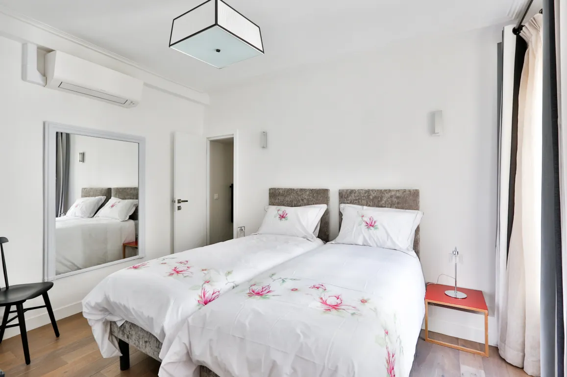 Élégante chambre moderne avec lits jumeaux, climatisation, miroir et décoration florale. Confort et design pour votre propriété de luxe.