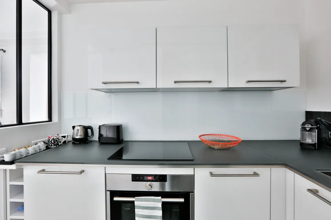Cuisine moderne blanche et épurée avec électroménager intégré, plan de travail foncé. Idéal pour appartement de luxe.
