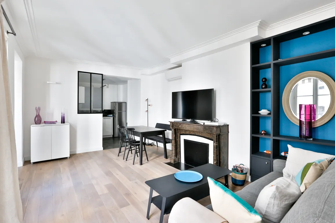 Salon moderne lumineux avec cuisine ouverte, cheminée, rangements intégrés bleus. Design contemporain pour appartement de luxe.