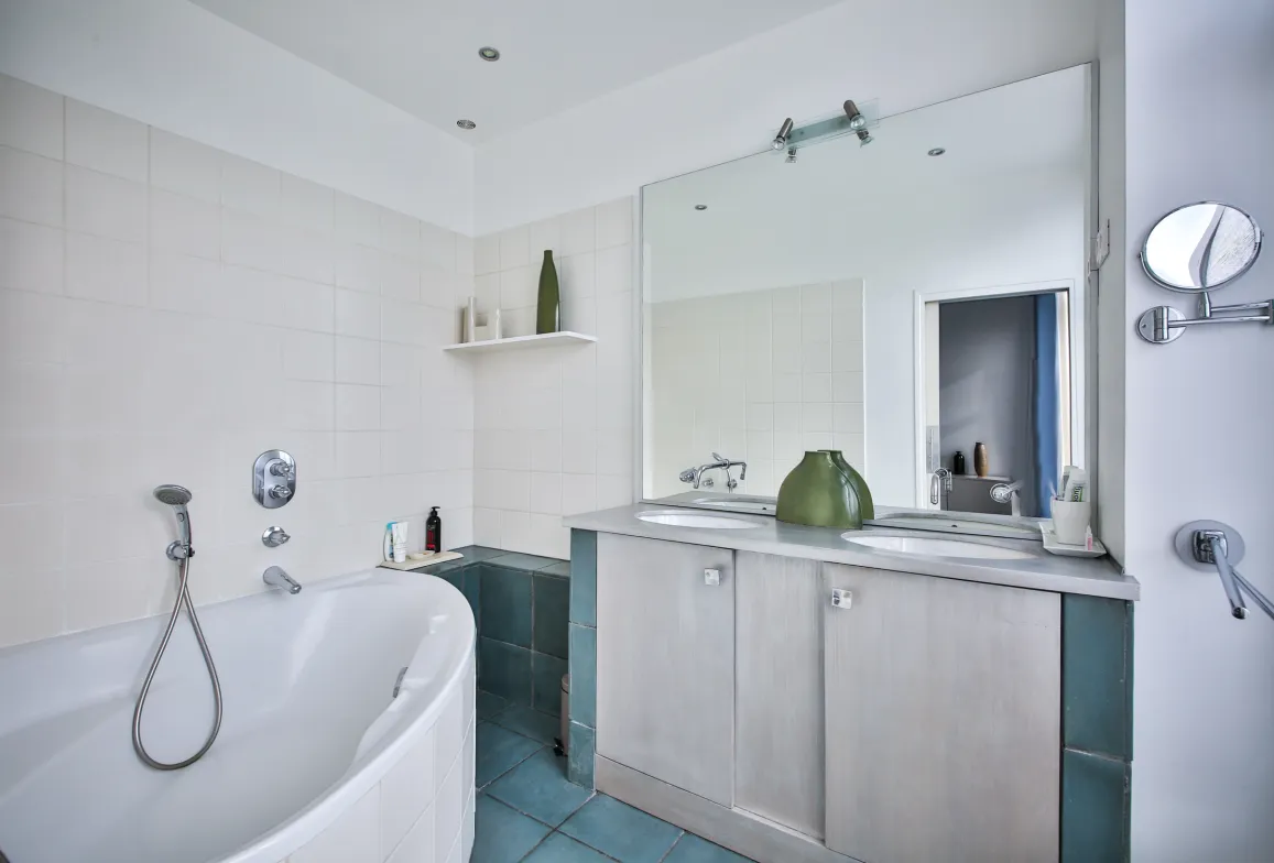 Salle de bain de luxe moderne: baignoire, double vasque, grand miroir, carrelage blanc/bleu. Design épuré, ambiance zen. Idéal propriété haut de gamme.