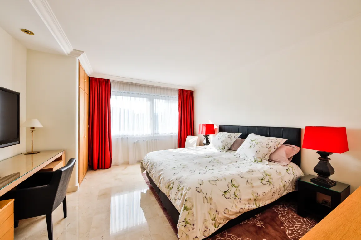 Splendide chambre de luxe avec lit king-size, rideaux rouges, sol en marbre, bureau et TV. Design moderne et lumineux.