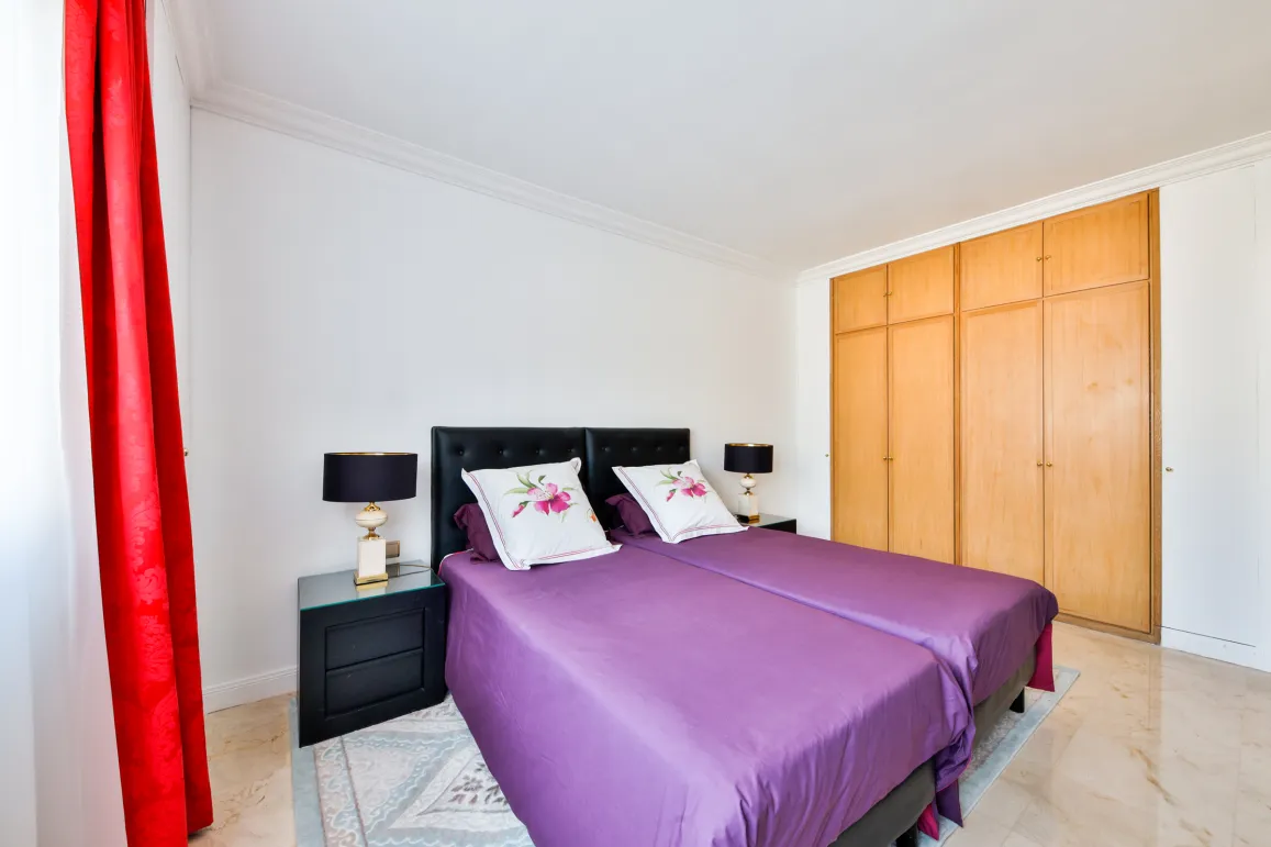 Chambre élégante avec lits jumeaux, literie violette, tables de chevet design et placards intégrés. Confort et style pour propriété de luxe.