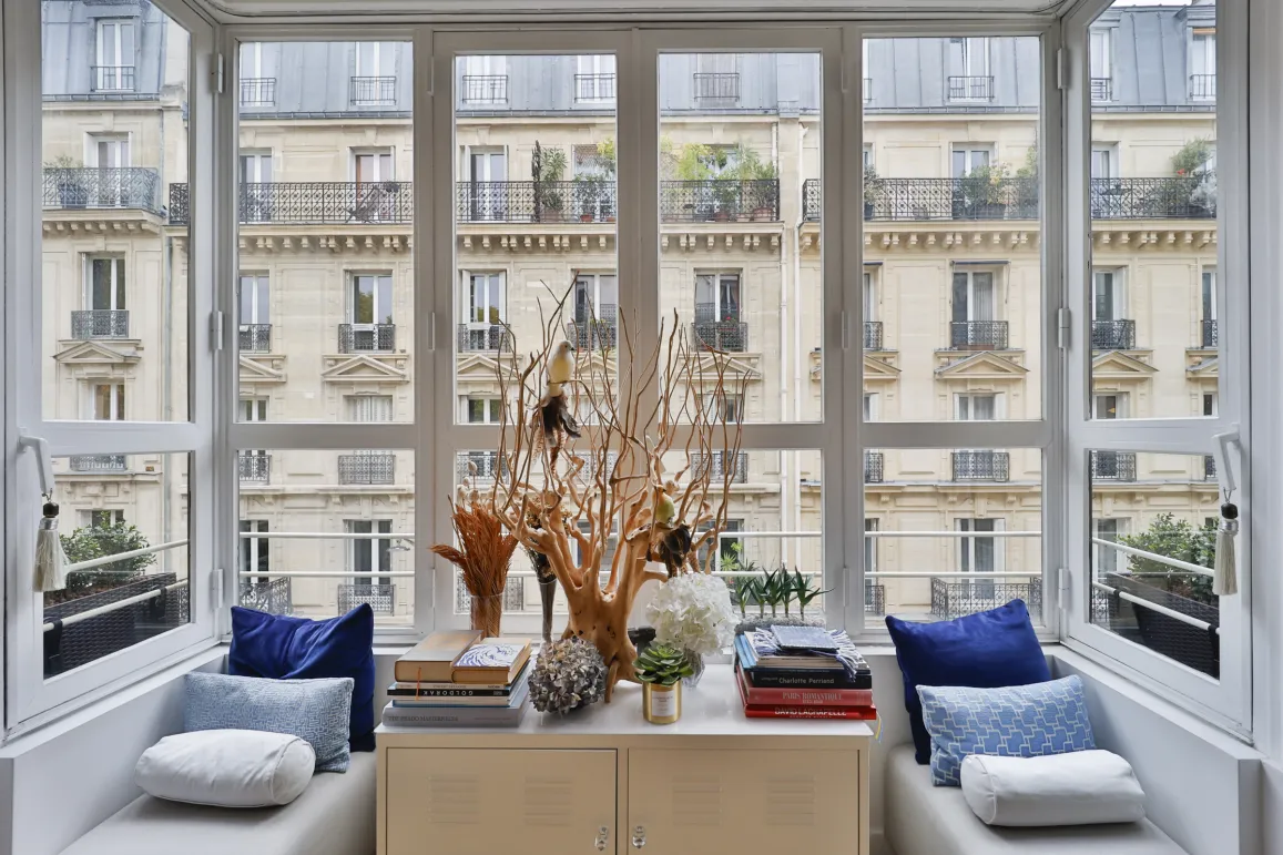 Appartement de luxe avec vue imprenable sur Paris. Fenêtre panoramique, coin lecture élégant, design intérieur raffiné. Lumière naturelle.