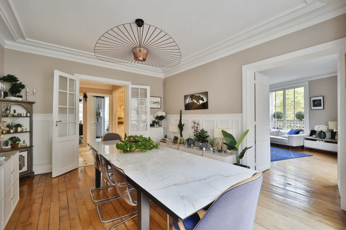 Magnifique salle à manger de luxe avec table en marbre, lustre design, parquet et moulures. Espace ouvert sur un salon lumineux. Élégance moderne.
