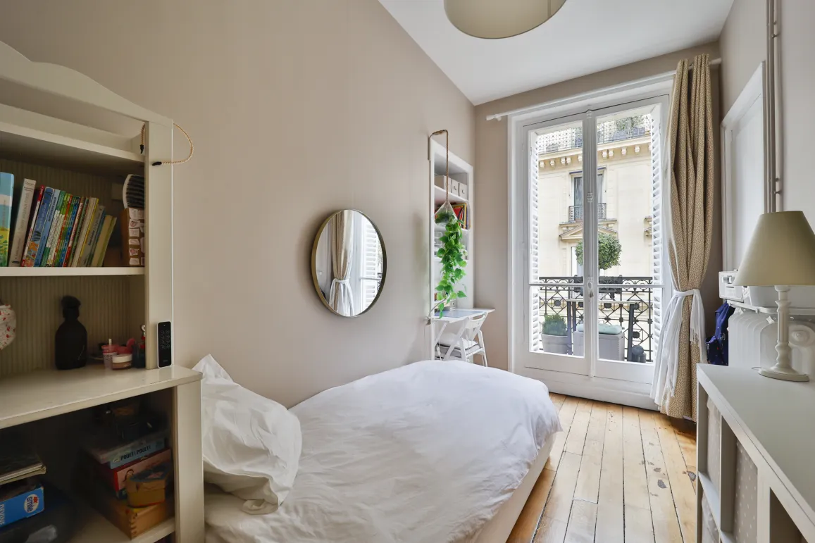 Chambre parisienne lumineuse avec balcon, parquet clair et vue dégagée. Lit simple, rangements intégrés. Idéal pour enfant ou bureau d'appoint. Charme et potentiel.
