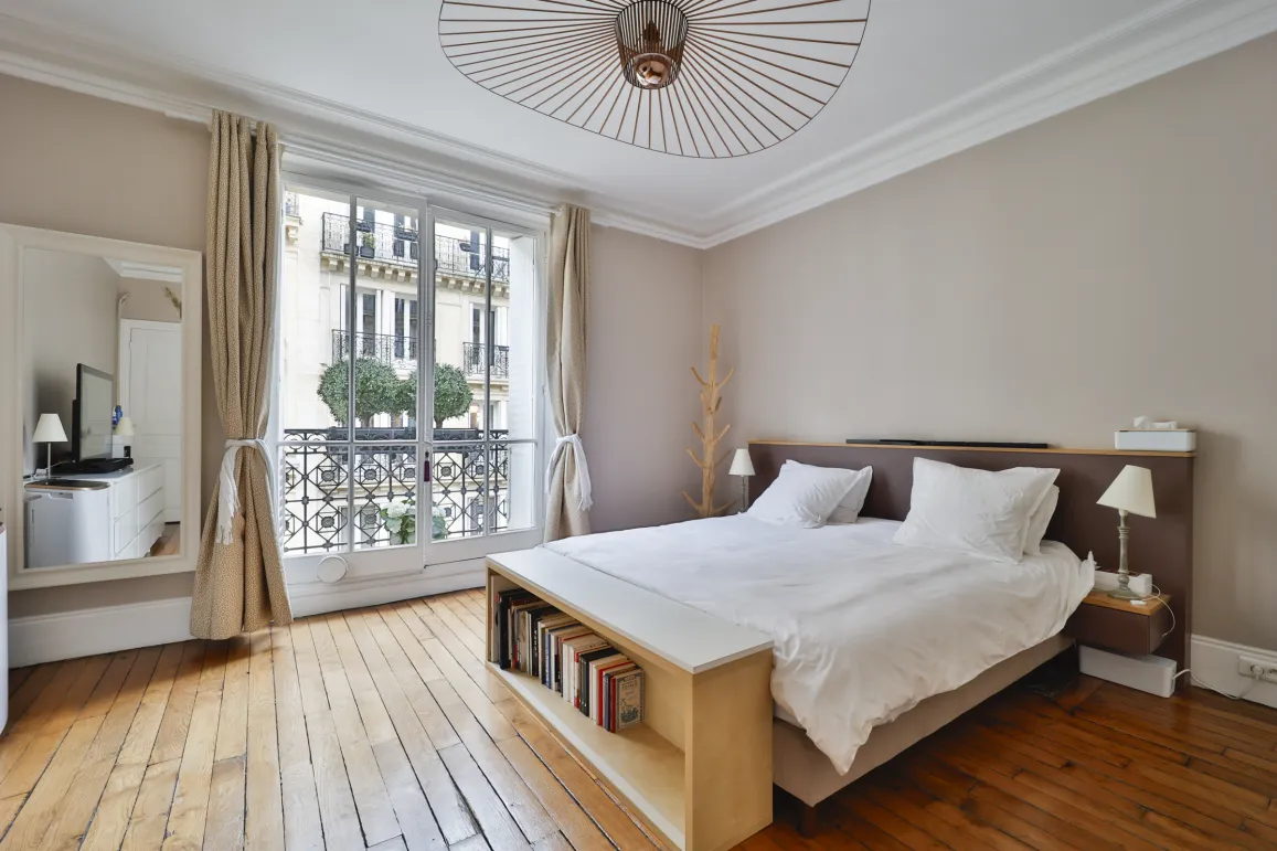 Chambre de luxe parisienne lumineuse avec parquet, balcon, vue Haussmannienne. Design moderne et élégant pour un appartement d'exception.