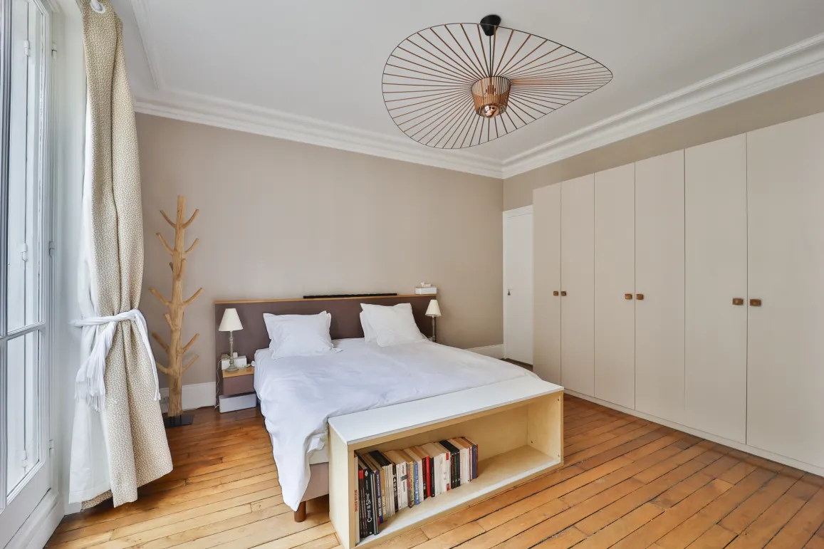 Chambre de luxe moderne et lumineuse avec parquet, rangements intégrés et luminaire design. Confort élégant pour un intérieur raffiné.