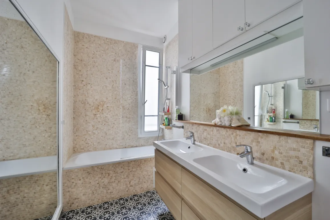 Salle de bain moderne et lumineuse avec double vasque, baignoire, carrelage élégant et miroir intégré. Design contemporain pour un confort optimal.