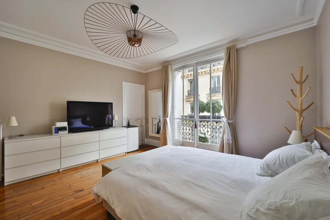Chambre luxe moderne, balcon, parquet, TV, luminaire design. Intérieur élégant et lumineux.