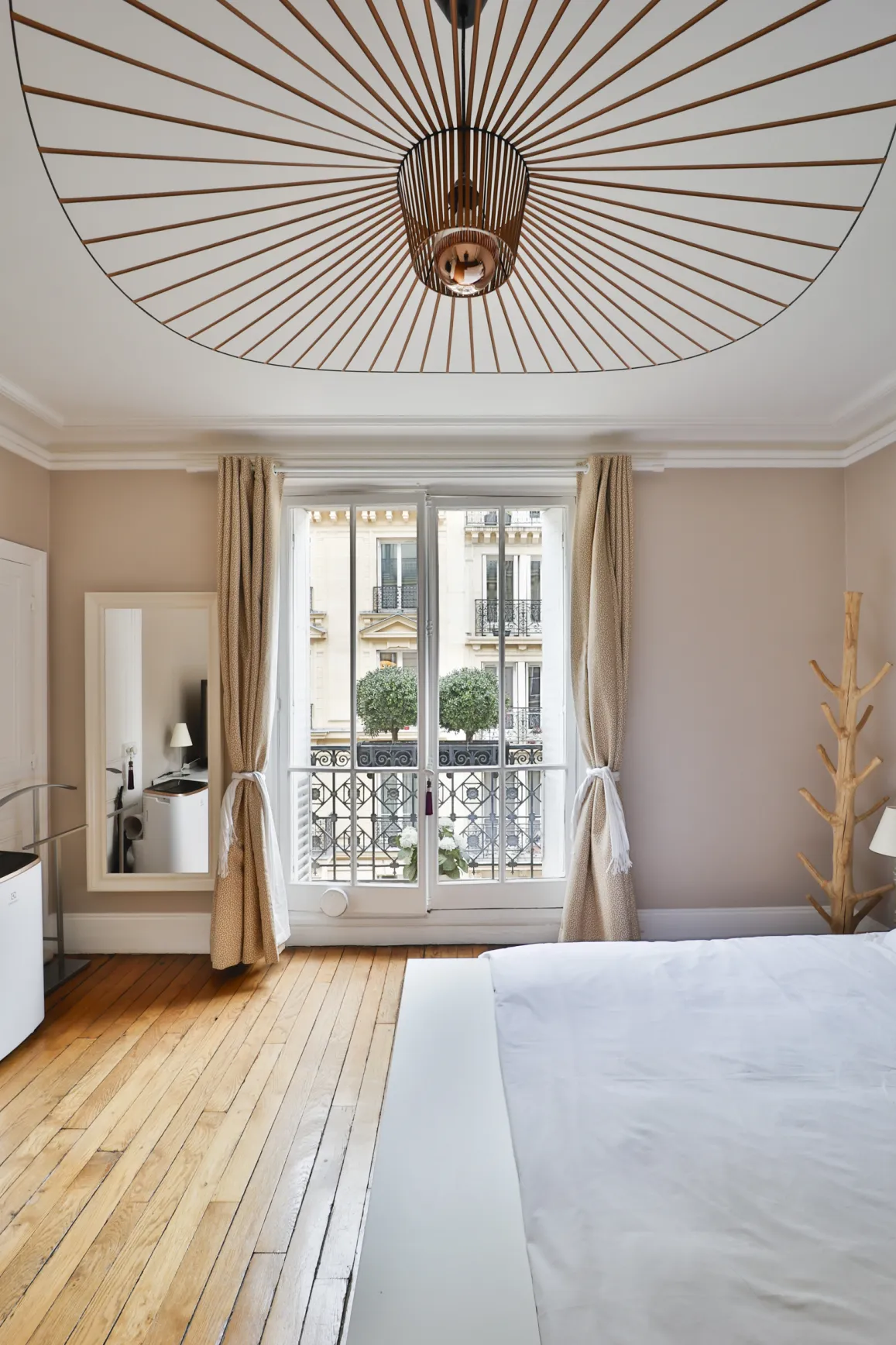 Chambre de luxe parisienne avec balcon, parquet, luminaire design. Élégance et vue urbaine pour un séjour raffiné.