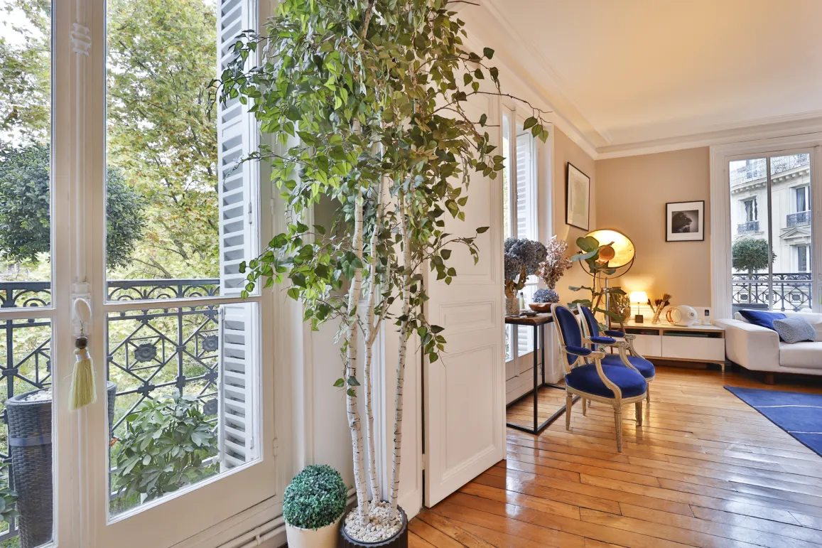 Salon lumineux et élégant d'un appartement de luxe avec vue verdoyante sur balcon. Parquet, mobilier chic et ambiance raffinée. Idéal Paris.