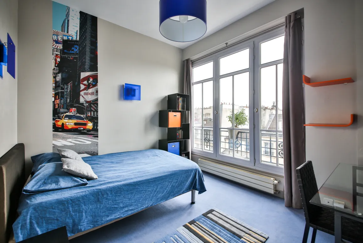 Chambre moderne et lumineuse d'un appartement de luxe. Lit confortable, vue ville, décoration urbaine chic avec fresque Times Square. Design contemporain.