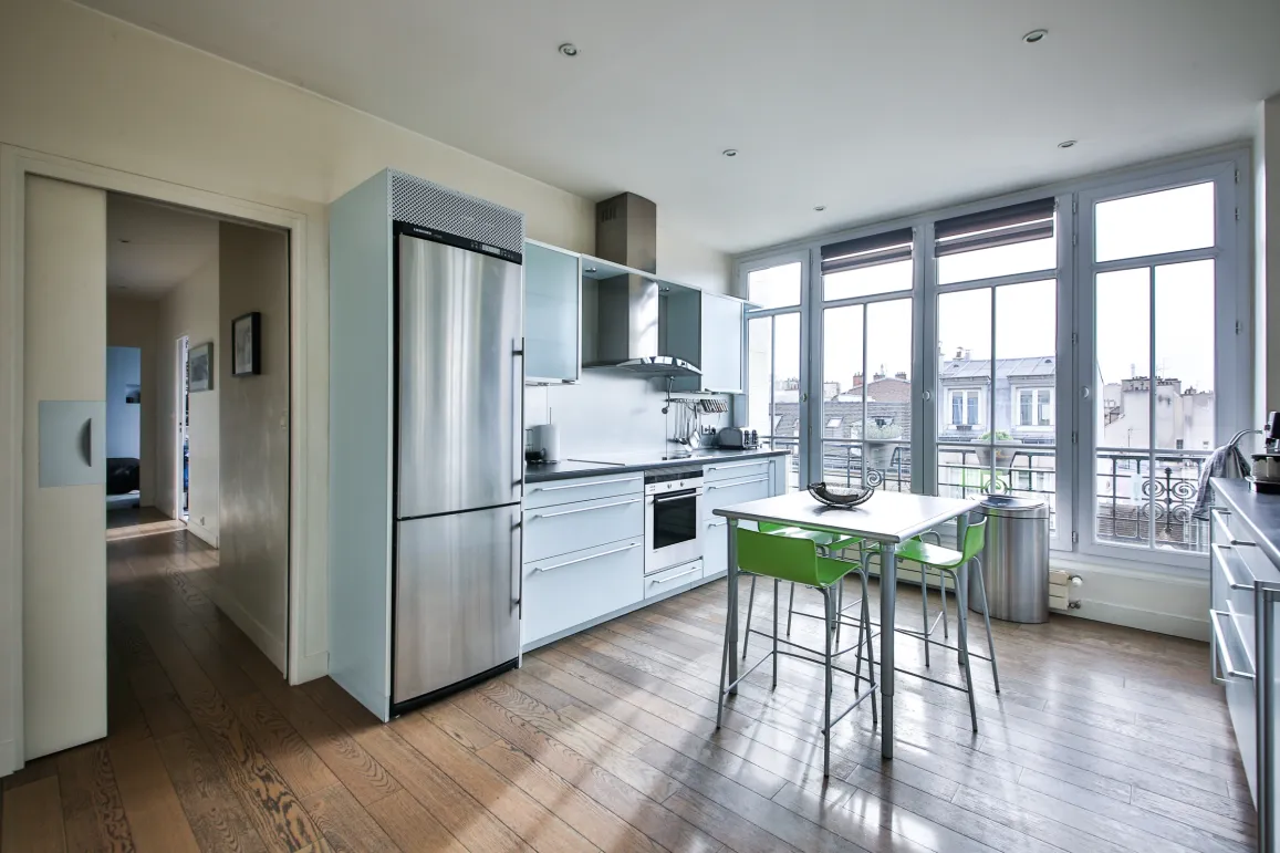 Cuisine design lumineuse, électroménager inox, parquet. Grandes baies vitrées avec vue ville. Appartement de luxe moderne et fonctionnel.