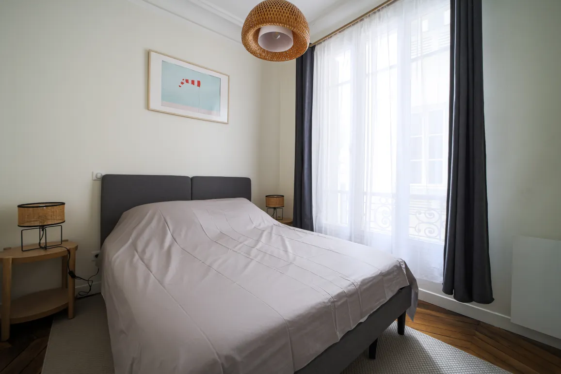 Chambre élégante et lumineuse avec lit double, décoration moderne et fenêtre offrant une belle lumière naturelle. Idéal pour un appartement de luxe.