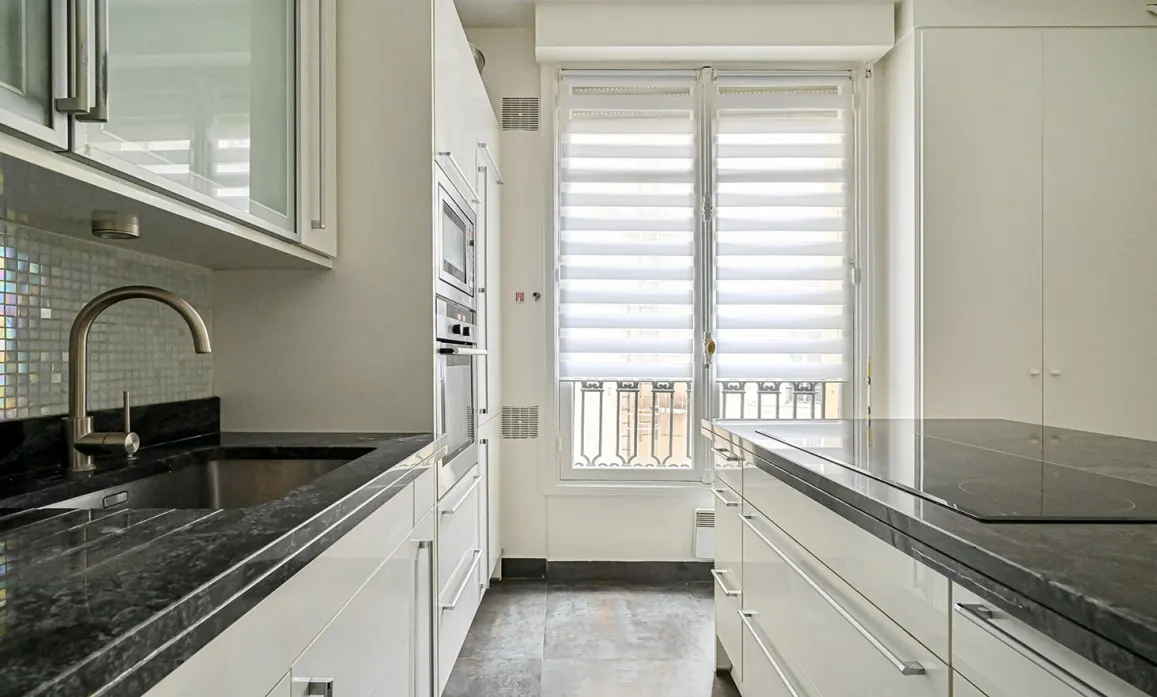 Cuisine de luxe moderne et lumineuse avec plans de travail en granit noir, équipements intégrés et grandes fenêtres. Idéal pour appartement de prestige.