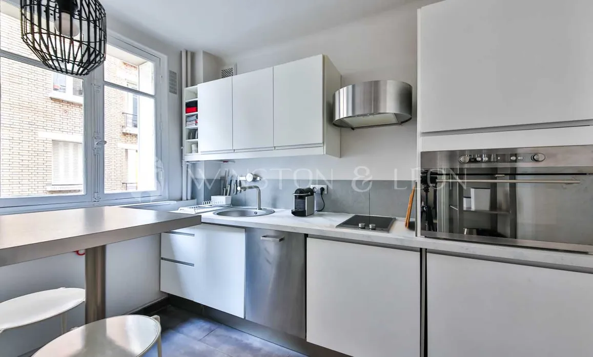 Cuisine moderne lumineuse, mobilier blanc épuré, électroménager inox intégré, coin repas. Design contemporain idéal pour appartement de luxe.