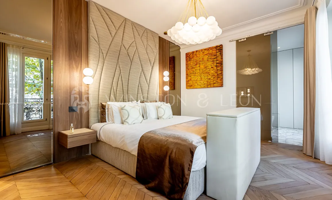 Chambre de luxe moderne avec tête de lit capitonnée, parquet chevron, éclairage design et touches artistiques. Élégance parisienne.
