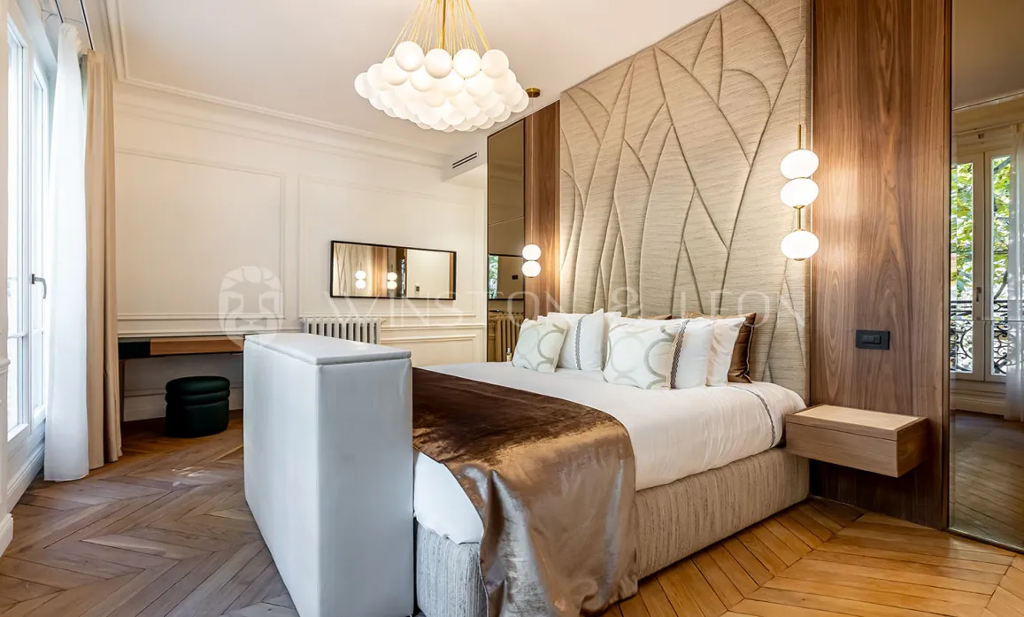 Chambre luxueuse au design contemporain et classique. Tête de lit texturée, parquet élégant, éclairage sophistiqué. Idéal pour immobilier haut de gamme.