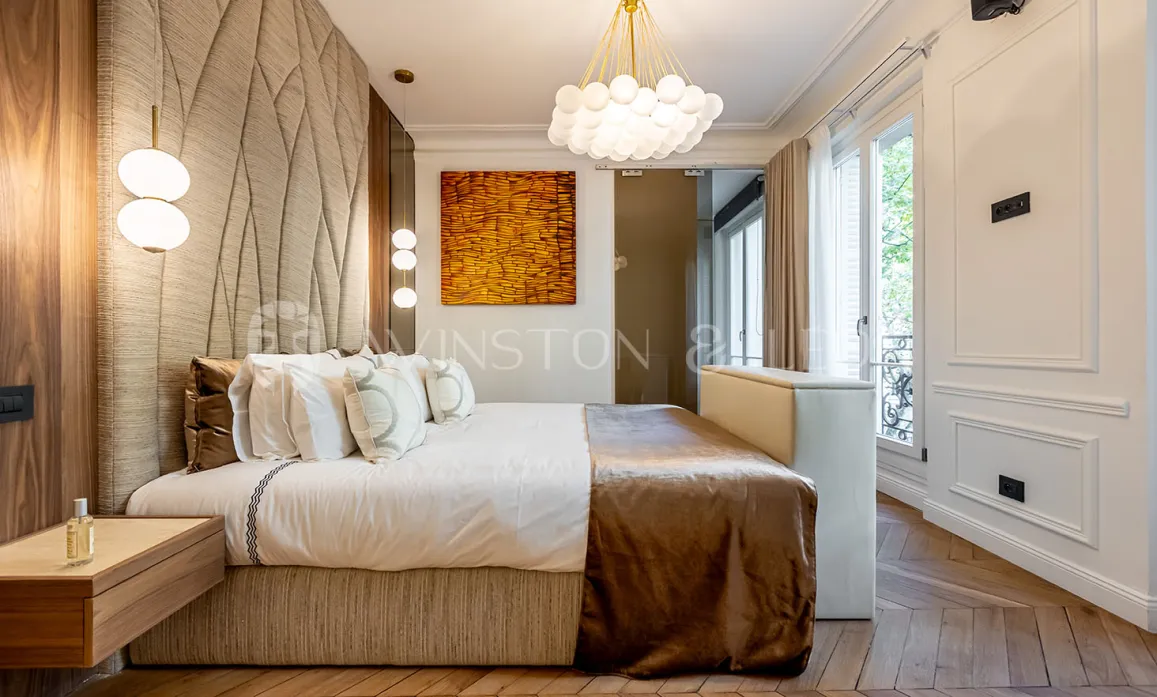 Chambre de luxe parisienne, design moderne, tête de lit texturée, parquet, éclairage élégant. Confort et style pour un appartement d'exception.