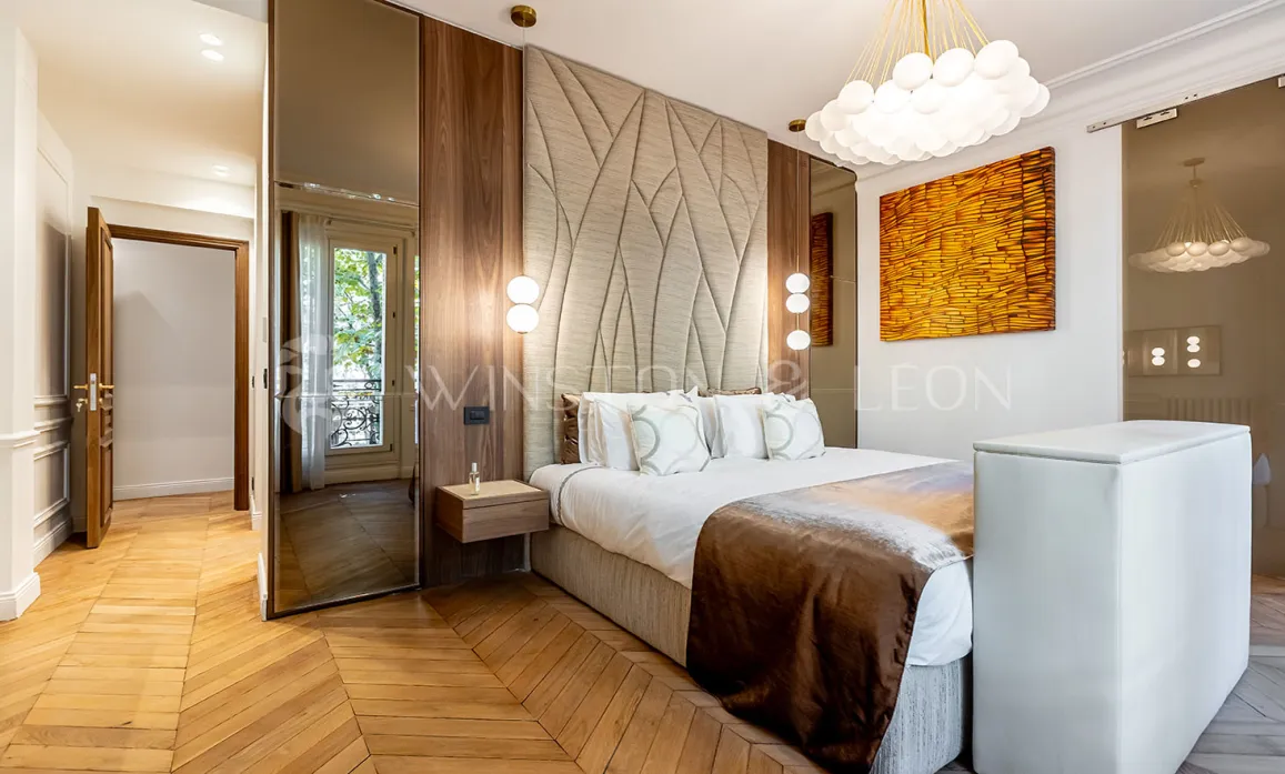 Chambre parentale luxe moderne: tête de lit design, parquet chevron, boiseries élégantes, éclairage contemporain. Ambiance raffinée et confort premium.