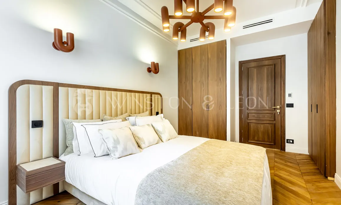 Chambre de luxe moderne avec tête de lit capitonnée, éclairage design, dressing intégré et parquet. Élégance et confort.
