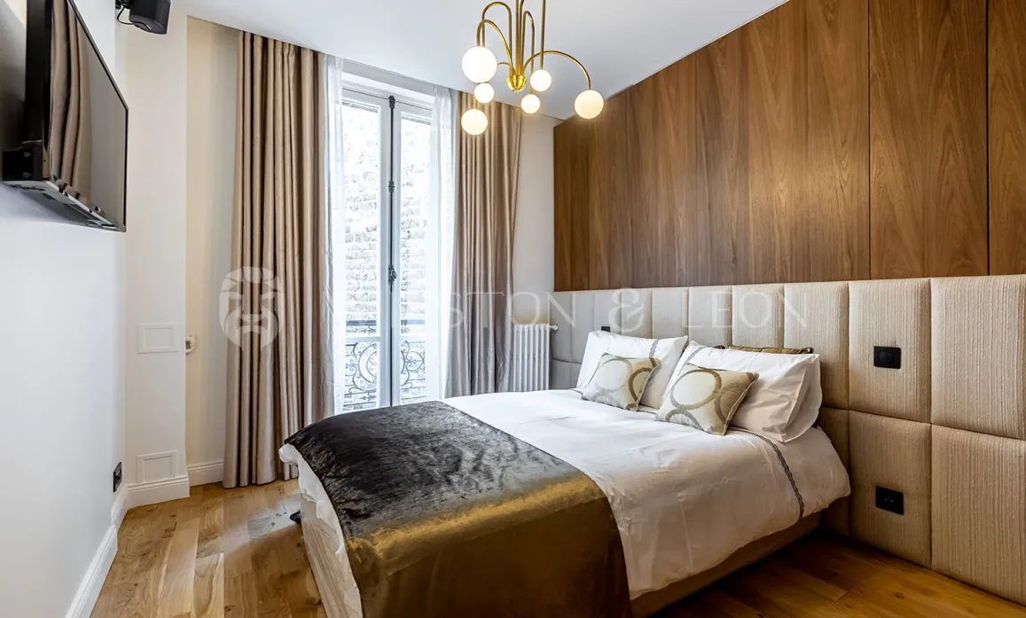 Chambre de luxe moderne avec boiseries murales, tête de lit rembourrée et lustre élégant. Confort et design contemporain pour un appartement parisien.