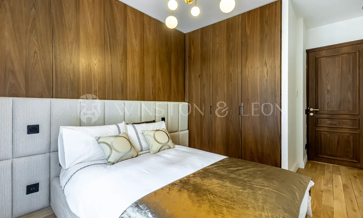 Chambre de luxe moderne avec boiseries murales élégantes, lit confortable et tête de lit capitonnée. Design raffiné pour suite parentale.