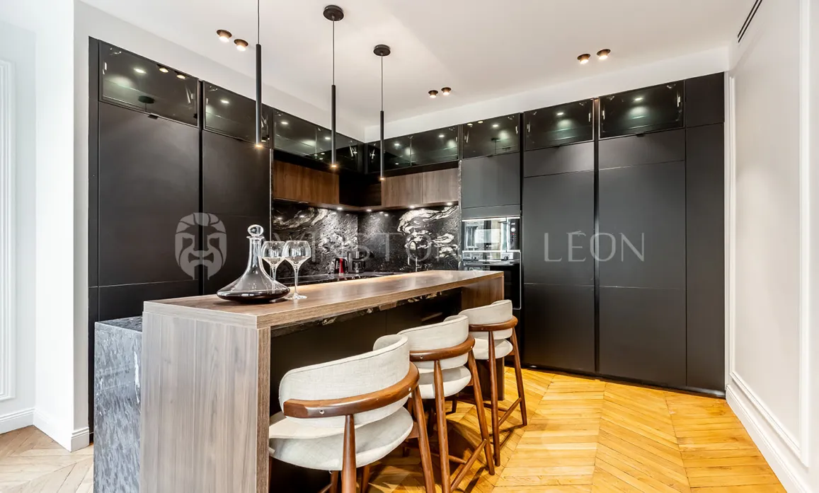 Cuisine de luxe contemporaine avec îlot bar, finitions noires mates, bois clair, marbre et parquet. Élégance et fonctionnalité.