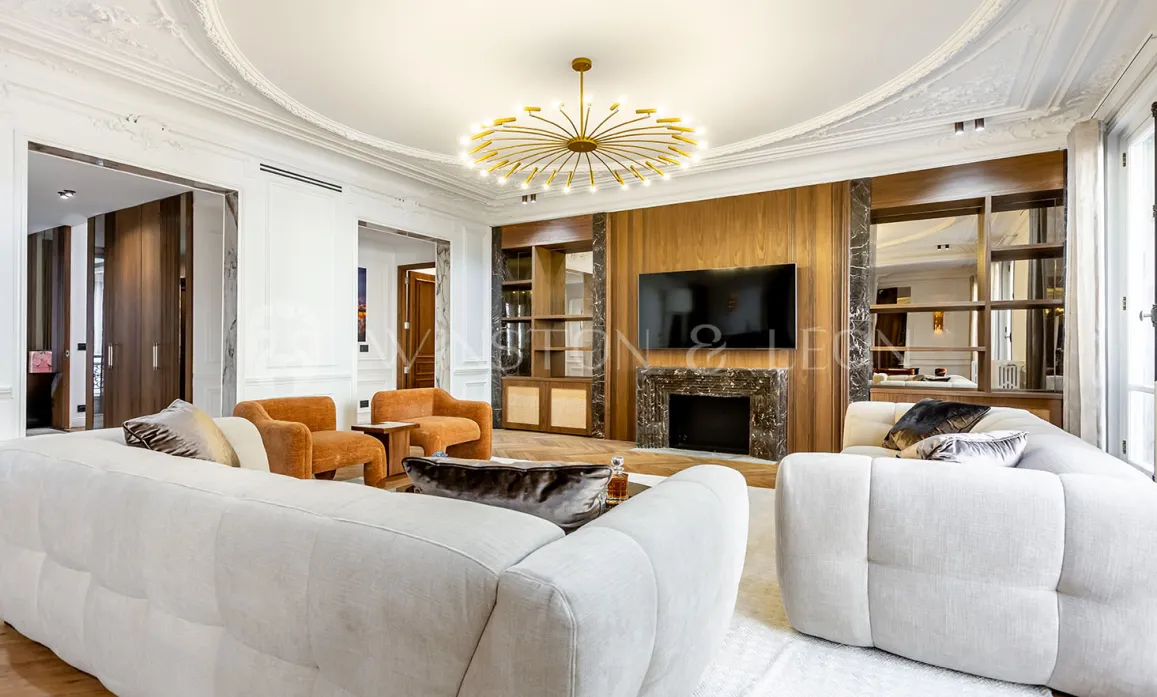 Salon de luxe contemporain avec cheminée marbre, TV intégrée, canapés blancs et lustre doré. Design intérieur élégant pour appartement prestige.