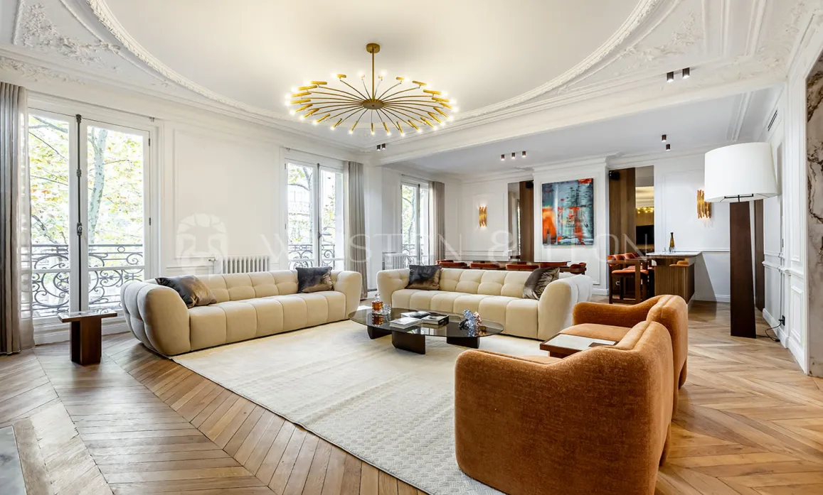 Grand salon de luxe haussmannien. Design contemporain, parquet chevrons, moulures élégantes et lustre moderne. Appartement de prestige.