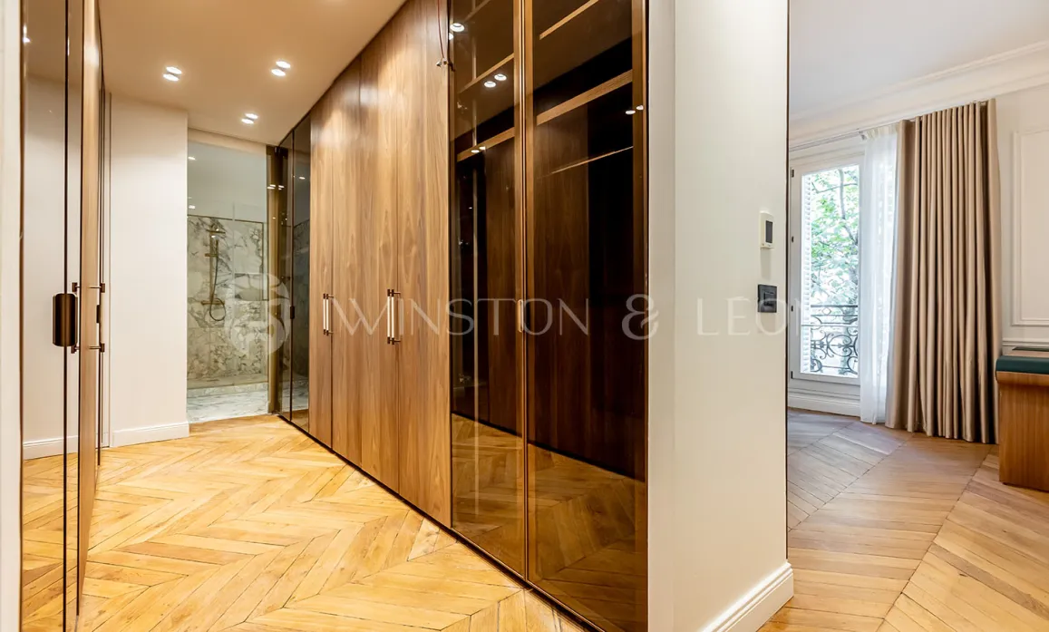 Luxueux dressing sur mesure en bois et verre, parquet chevron. Salle de bain attenante. Design élégant pour un appartement de prestige.