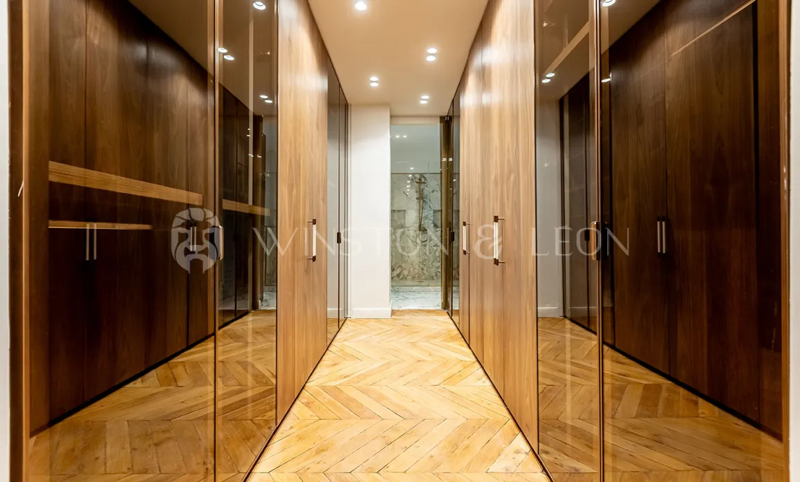 Dressing de luxe moderne avec placards en bois et verre, parquet chevrons. Rangement élégant pour propriété haut de gamme.