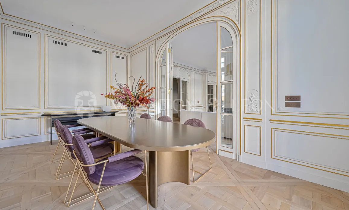 Élégante salle à manger de luxe parisienne. Boiseries dorées, parquet, table design moderne, chaises velours. Raffinement Haussmannien.