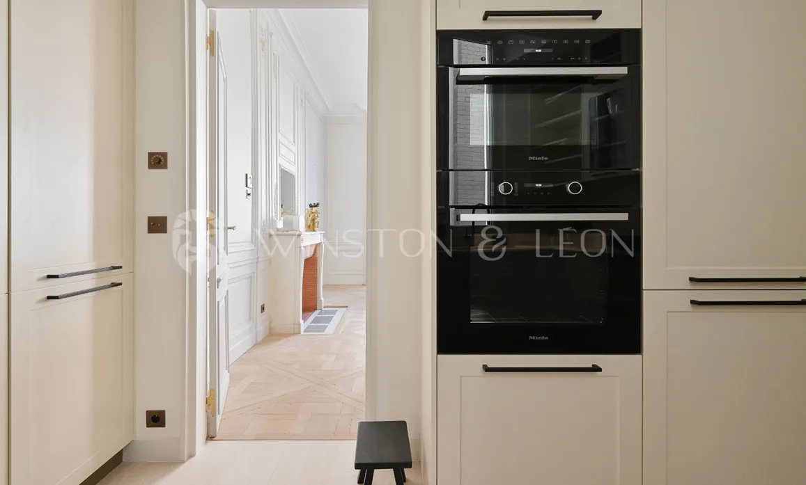 Cuisine Miele moderne et élégante, ouvrant sur un salon Haussmannien. Appartement de luxe rénové à Paris.