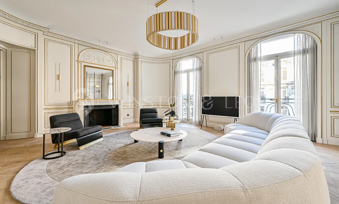 Salon de luxe parisien. Design moderne et classique Haussmannien, moulures dorées, canapé contemporain. Élégance et raffinement.