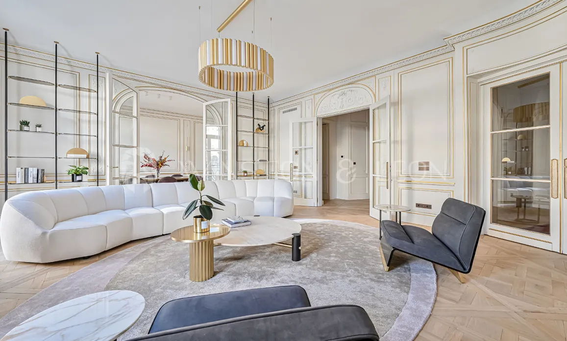 Salon de luxe contemporain, moulures dorées, canapé design, parquet chevrons. Élégance parisienne lumineuse et raffinée.