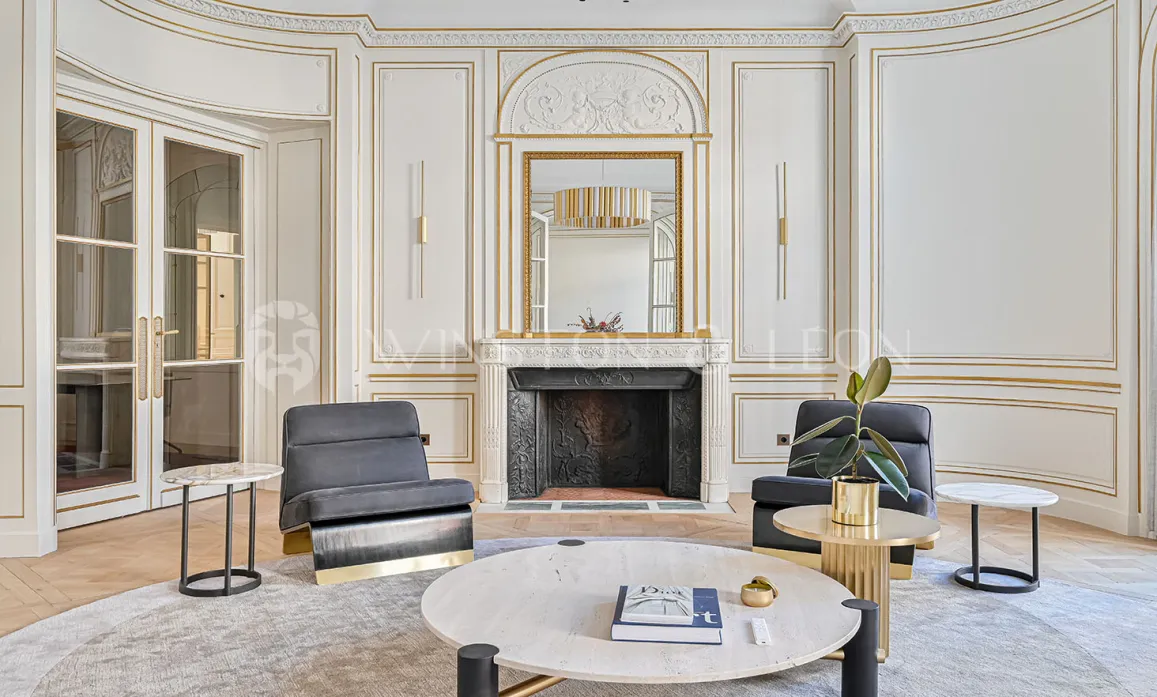 Appartement de luxe parisien, salon Haussmannien raffiné avec boiseries dorées, cheminée marbre et mobilier contemporain chic.