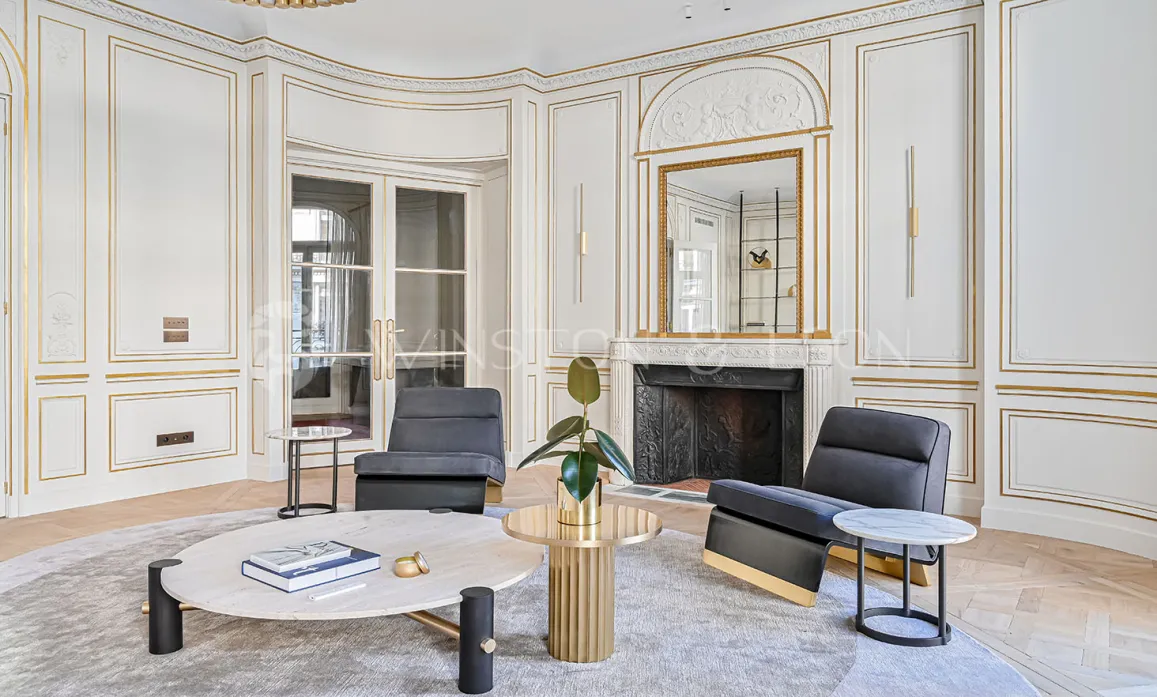 Luxueux salon parisien Haussmannien. Moulures dorées, cheminée, mobilier design contemporain. Élégance et raffinement intemporels.