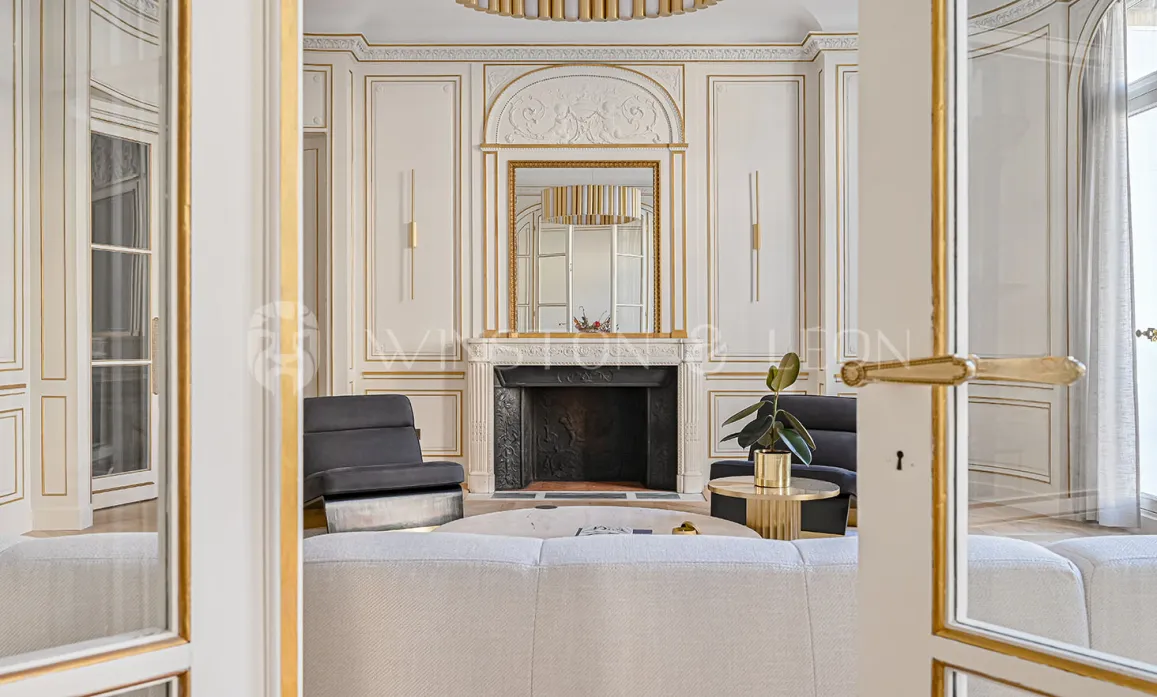 Salon de luxe parisien avec moulures dorées, cheminée classique et mobilier élégant. Un intérieur prestigieux alliant charme ancien et design moderne.