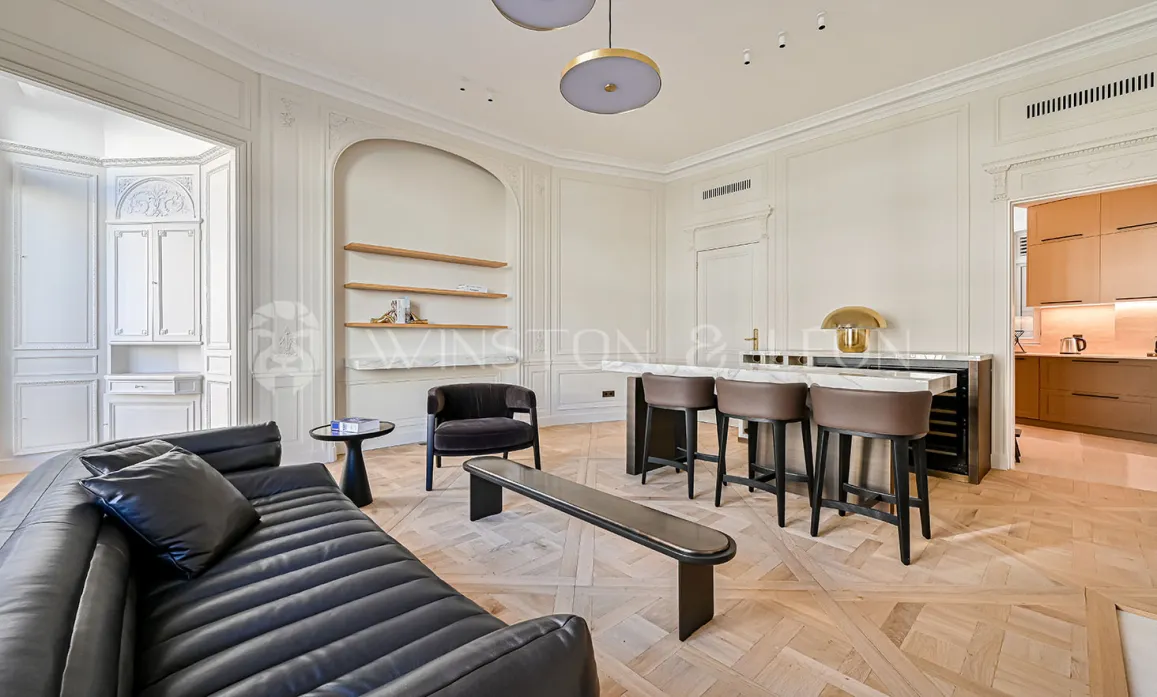 Superbe salon de luxe parisien. Design contemporain, parquet Versailles, moulures élégantes, bar intégré et cuisine moderne. Ambiance raffinée et lumineuse.