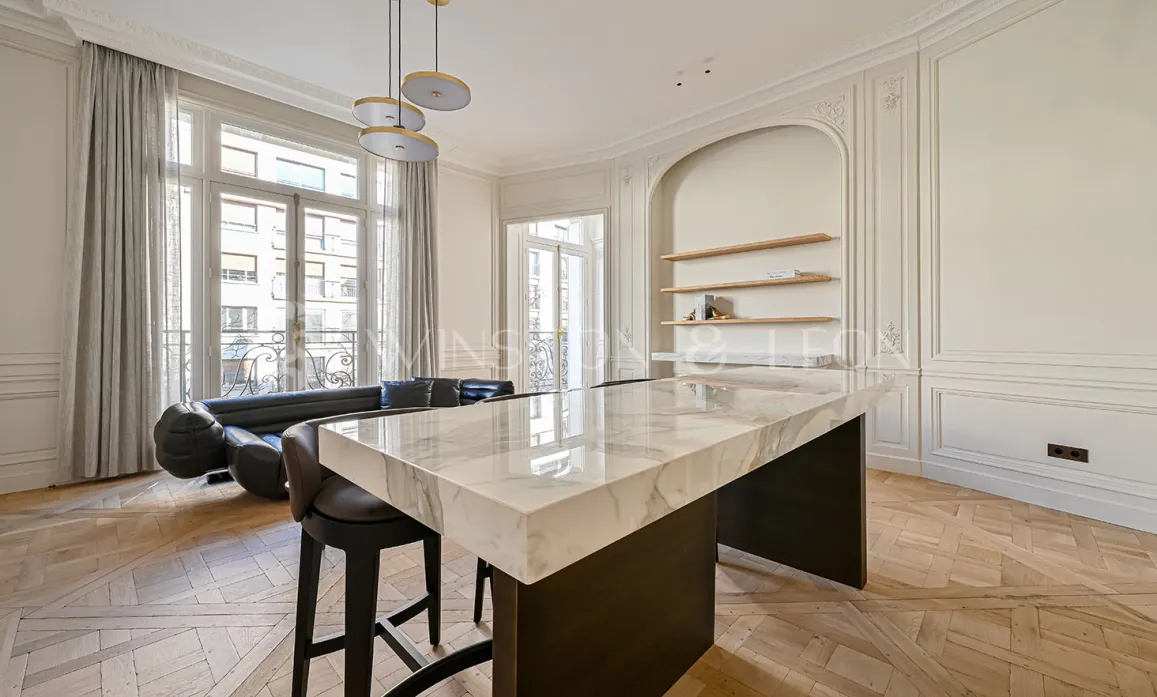 Appartement de luxe Parisien avec cuisine ouverte design, îlot en marbre, parquet chevron et moulures. Élégance et modernité.