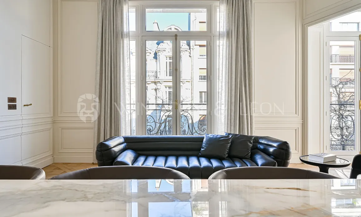 Salon de luxe parisien avec canapé cuir noir, moulures élégantes et vue haussmannienne. Design contemporain et raffinement.