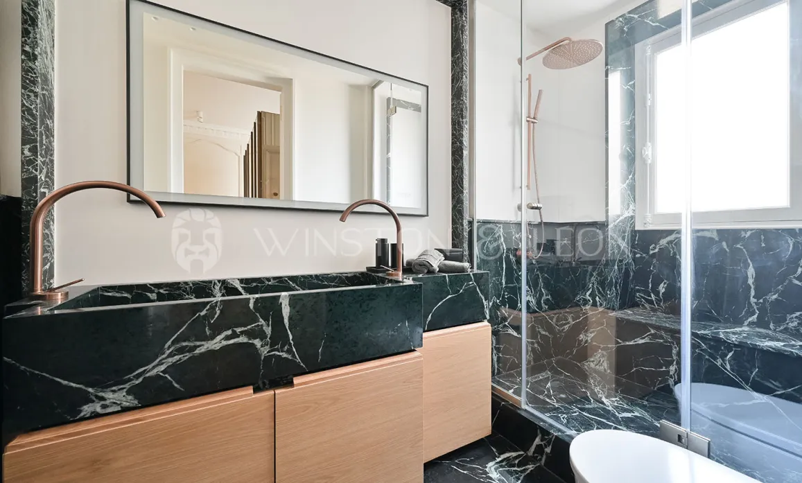 Salle de bain de luxe. Marbre noir veiné blanc, double vasque bois clair, robinetterie cuivre. Douche italienne moderne. Élégance et raffinement.